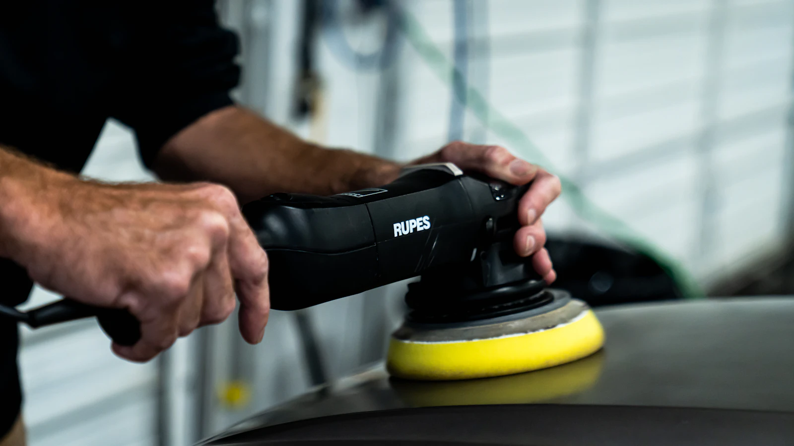 A professional detailer machine-polishing a car panel in a garage